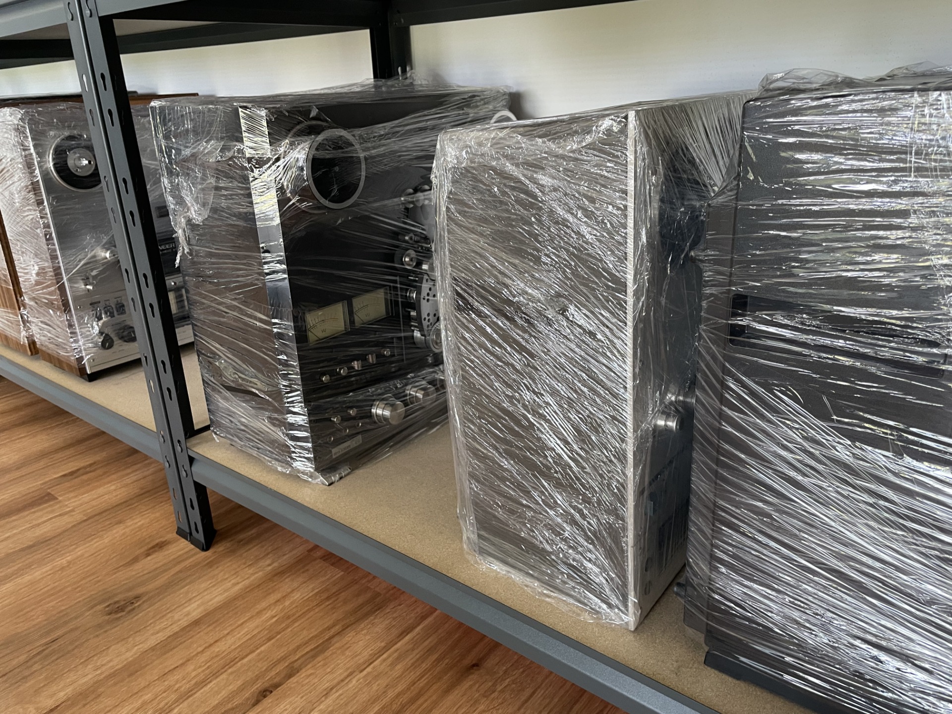 Technics RS-1700 zabalený do průhledné fólie na kovových regálech v skladu.
