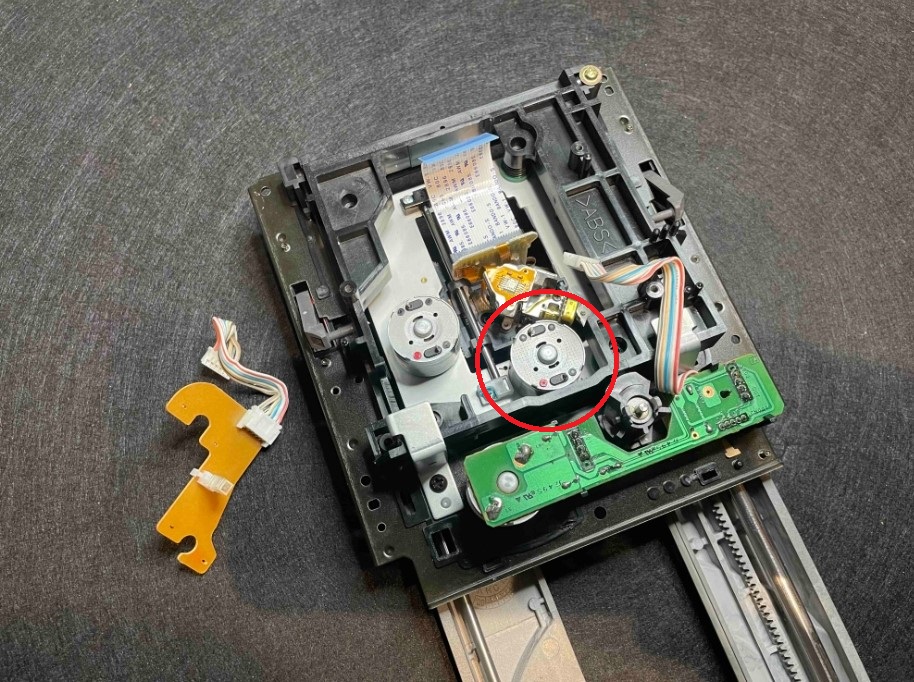 Vadný spindle motor RF320CH-12400. Demontáž původního spindle motoru vyžaduje stažení originálního unašeče disku, který bývá po letech provozu velmi pevně usazen na hřídeli motoru. Celý proces vyžaduje speciální přípravky a maximální opatrnost, aby nedošlo k poškození mechaniky nebo změně geometrie transportu.